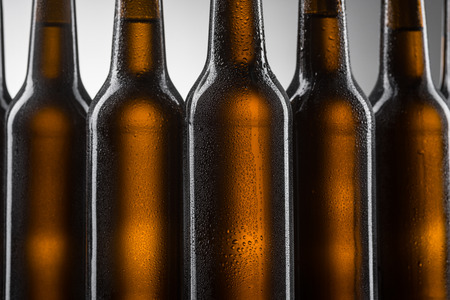 Close up of beer bottles on grey background. Row of dark brown bottles covered with condensate. Water drops on glass.の写真素材