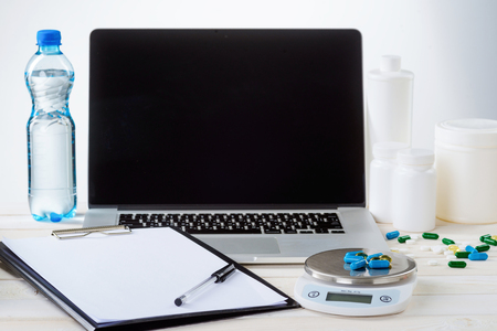 Bottle of water, dietary supplements, a laptop. note paper, a pen and a food scale, close-up. White background. Balanced approach to weight loss.の写真素材