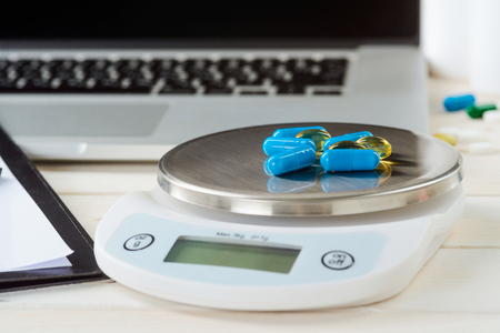 Pills and a food scale on the light wooden table, close-up. Laptop on the background. Vitamins and supplements.の写真素材