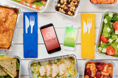 Smartphones indicating bad and good BMI results. Pie, cheese sandwiches, rice and chicken, nuts and dried fruit, tomato salad, plums and tangerines. Healthy and unhealthy food options.の写真素材