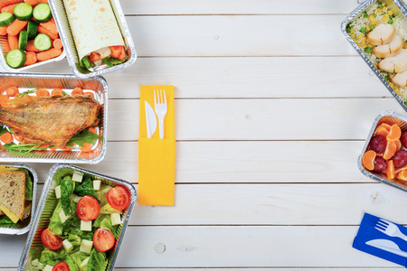 Cheese sandwich, a vegetable roll, fish, tomato and lettuce salad, plastic cutlery, rice with chicken, tangerines and plums on the wooden surface. Place to insert your text. Takeout food.の写真素材
