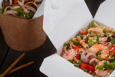 Chinese take-away food. Selective focus on opened box full of stir-fried rice with seafood and vegetables. There are another take-out box and chopsticks in the background.の写真素材