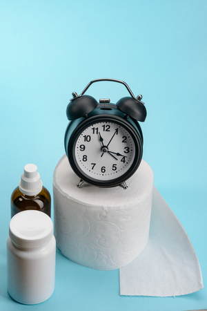 Toilet paper, alarm clock and medicine pills on blue background. Constipation and medical treatment.の写真素材