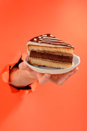 Hand serving a chocolate cake through a torn hole in red paper background.の写真素材