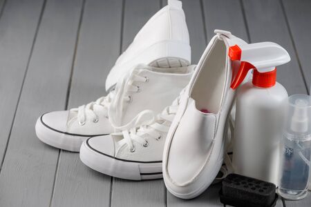 Care for canvas and leather footwear. White sneakers and loafers, cleaner spray and brush on gray wooden background.の写真素材