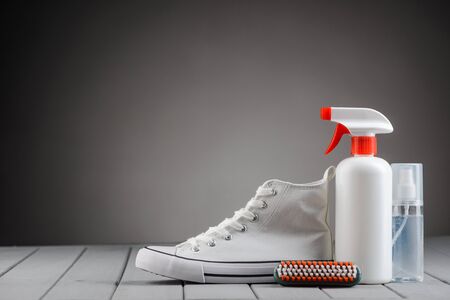 White canvas sneaker and footwear care supplies on gray background with copy space. Cleaning and...