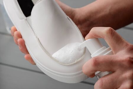 Man cleaning white leather shoes, close up on hands. Usinf a spray. Proper care for footwear to save a good look.の写真素材