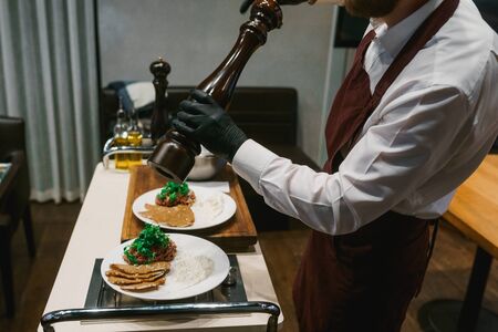 Chef seasoning dishes with a pepper mill, cooking in front of restaurant's visitors.の写真素材