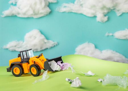 Yellow toy truck collecting trash scattered over green hills. Ecology art project made by child.