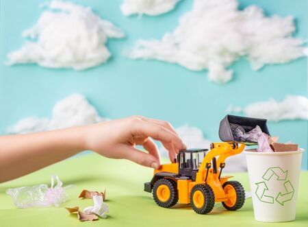 Child playing with a toy truck and loading garbage into the bin with recycle sign. Cleaning environment, care for planet and ecological awareness.の写真素材