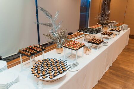 White table with diverse appetizers and tableware served by catering company. Gourmet food at...