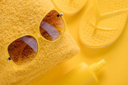 Stylish yellow sunglasses advertisement, flat lay. Folded towel, flip-flop sandals and sunscreen spray.の写真素材