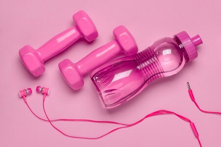Dumbbells, bottle and headphones on pink background, flat lay. Sport and music accessories.の写真素材