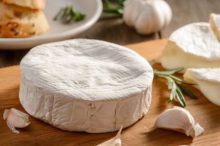 Wheel of Camembert cheese, garlic and rosemary on a wooden backgroundの写真素材
