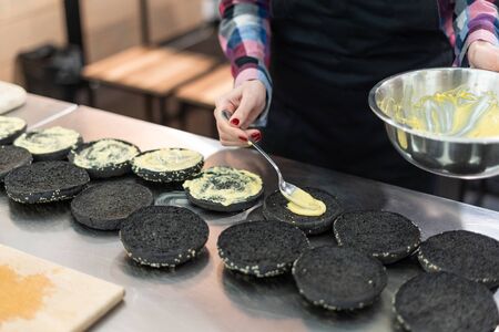 Woman putting cheese sauce onto black bunsの写真素材