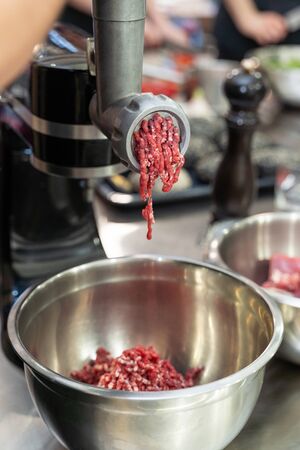 Minced raw meat coming out of an electric grinder. Making ground beef with modern kitchen equipment.の写真素材