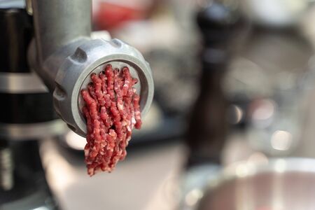 Close-up on minced meat coming out of an electric grinder. Modern food processing with convenient kitchen tools.の写真素材