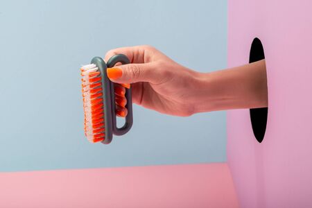 Close-up on womans hand holding a brush on blue and pink background