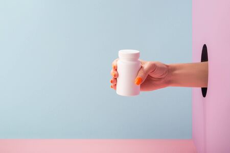 Womans hand holding a white bottle of pills on blue and pink backgroundの写真素材