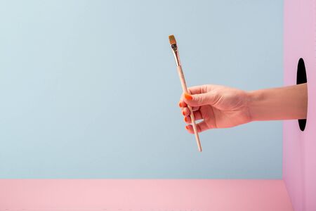Womans hand holding an art brush on blue and pink backgroundの写真素材