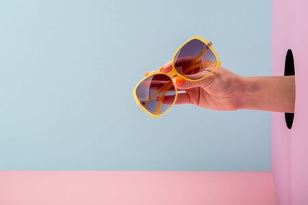 Womans hand holding yellow eyeglasses on blue and pink backgroundの写真素材