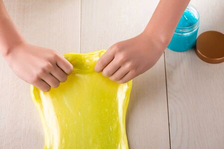 Girl kneading yellow slime, playing with it while blue one is in a jarの写真素材