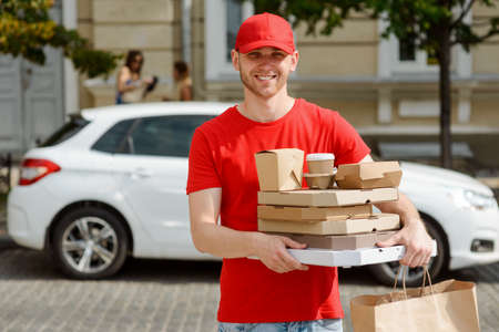 Delivery man loves his job. Cheerful young man carrying paper containersの写真素材