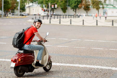 Delighted man, wearing a backpack and a helmet, driving a motorbikeの写真素材