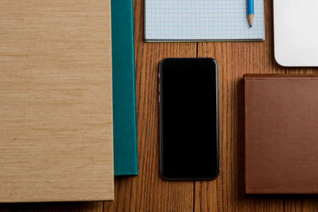 Phone beside books, laptop and office supplies on the wooden tableの写真素材