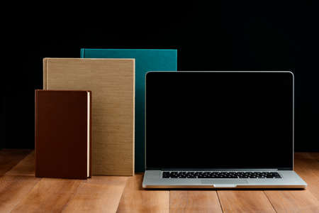 Hardcover books and laptop on wooden desktop