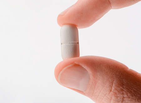 Close up on white pill between two fingersの写真素材