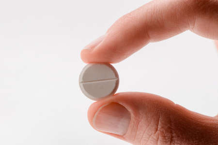 Close up on a white tablet pill between two fingersの写真素材