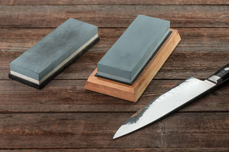 Japanese knife and two sharpenning stones on rustic wooden backg