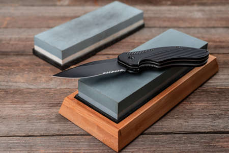 Close-up on a pocket knife laying on a whetstone on rustic woodeの写真素材