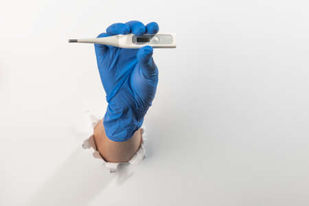 Hand in a latex glove holding a thermometer through torn white wall