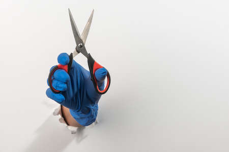 Hand in a latex glove holding scissors through torn white wallの写真素材