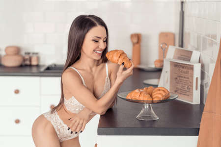 Young seductive woman in white lace underwear eating a fresh croissantの写真素材
