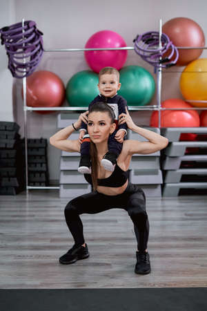 Mother doing squats with her kid in the gym