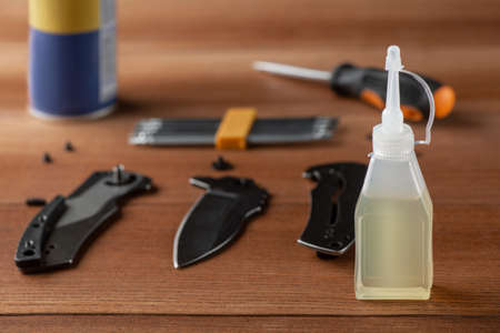 Bottle of household oil, parts of a disassembled knife and tools on wooden table. Lubricating knife...