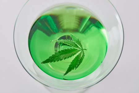 Close top view on a glass of a green cocktail with a cannabis leaf floating