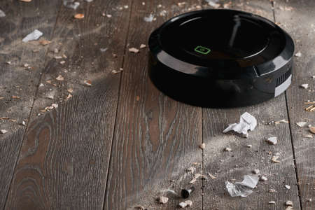 Balck robotic vacuum cleaning wooden floor from dust and rubbish