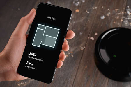 Man using an app on his phone to control a robotic vacuum cleane