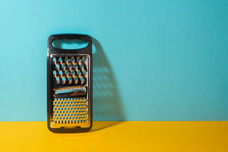 Stainless steel grater with plastic handle on yellow and blue backgroundの写真素材