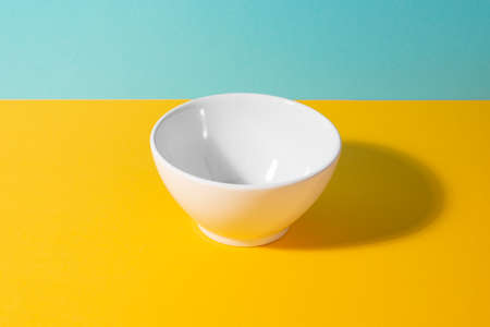 Empty white ceramic bowl on yellow and blue backgroundの写真素材