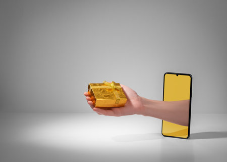 Hand giving a beautiful golden gift box from out of phone screenの写真素材
