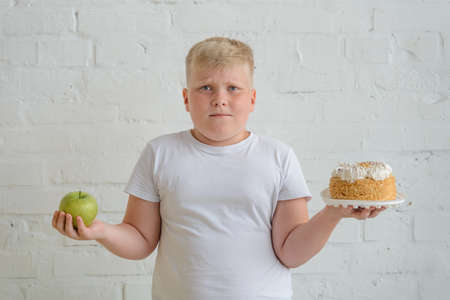 Boy choosing between apple and cake, studio portrait on whiteの写真素材