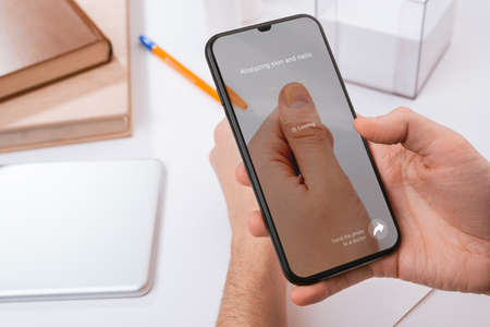 Man using a phone to recognize a problem with his nailの写真素材