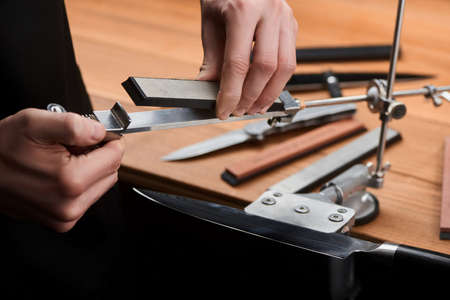 Close-up on hands inserting a whetstone into a manual sharpener machine. Fine and precise sharpening for a Japanese knife.の写真素材