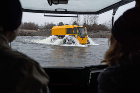 Couple watching at a yellow off-roader crossing a riverの写真素材