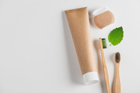 Top view on toothpaste, bamboo toothbrushes, dental floss and a leaf